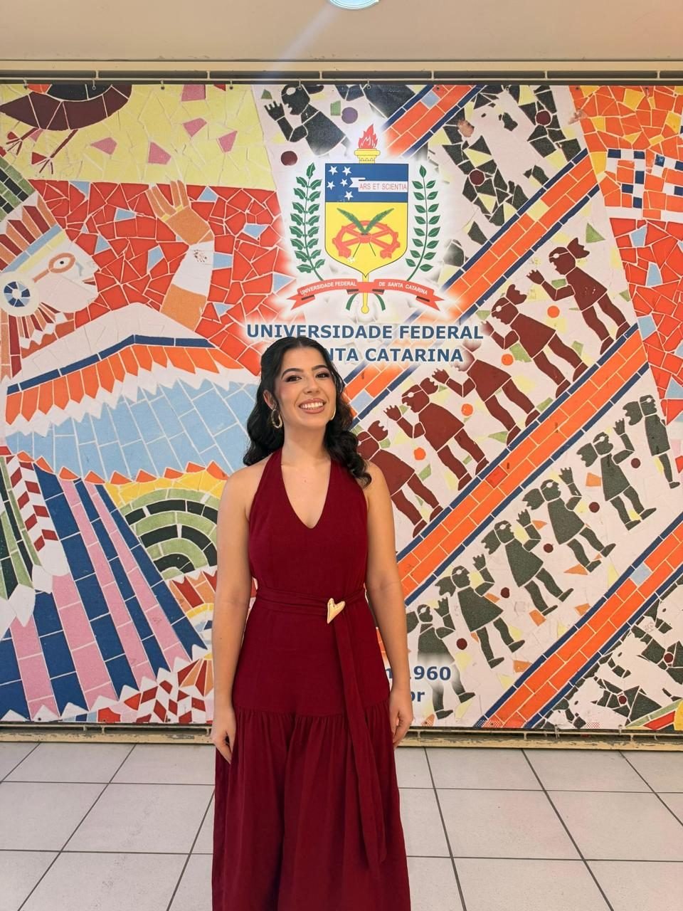 Bia de vestido vinho em frente a um mural colorido de mosaico.